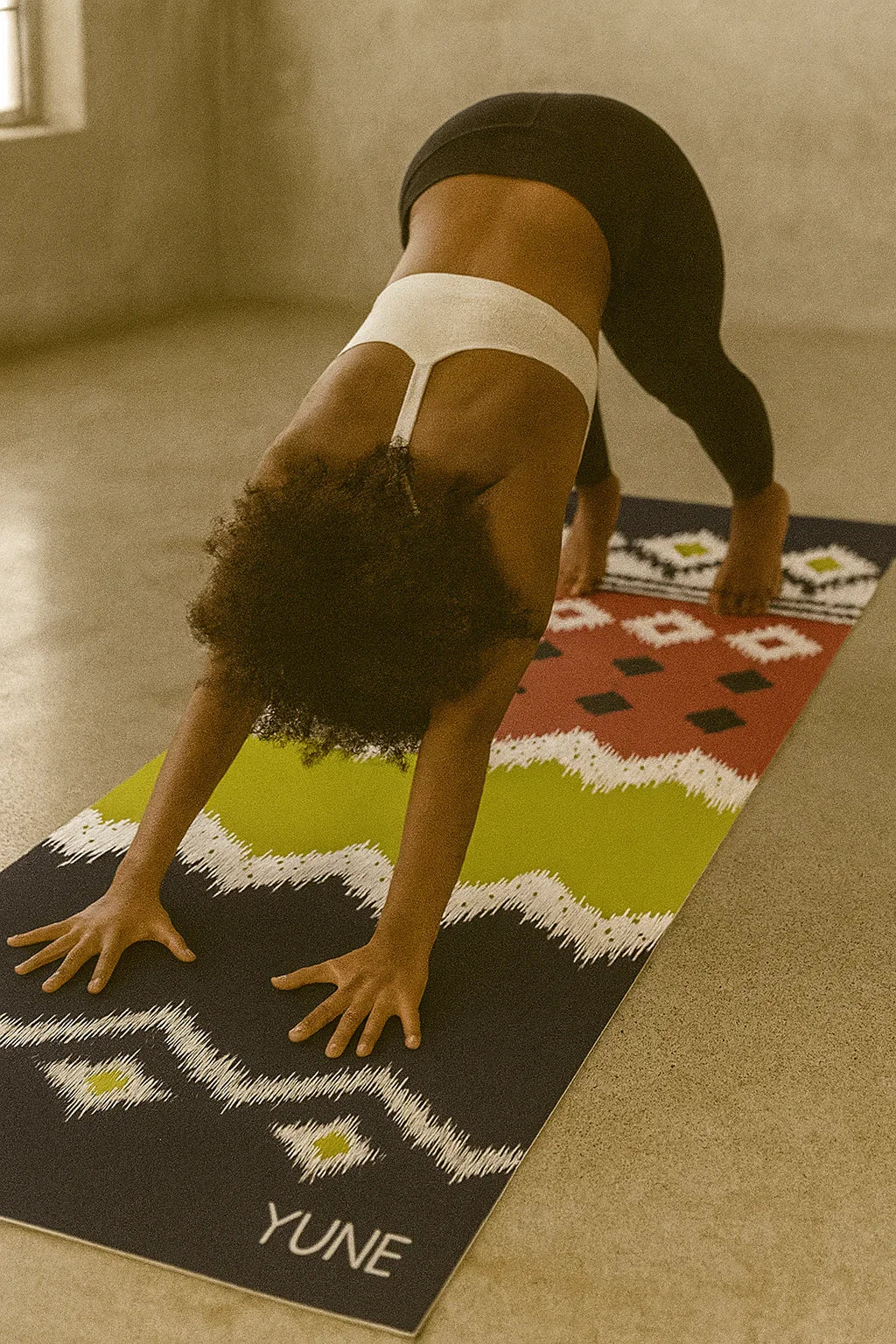 Person practicing yoga on a colorful mat with 'YUNE' branding in a studio setting.