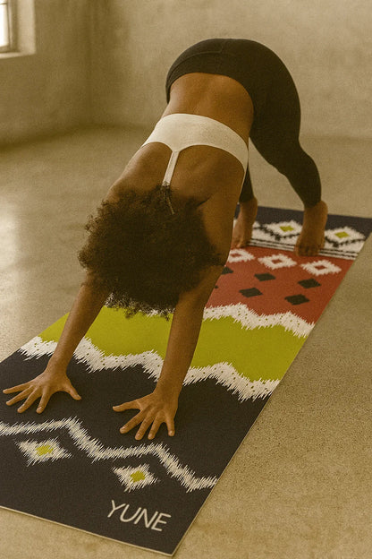 Person practicing yoga on a colorful mat with 'YUNE' branding in a studio setting.