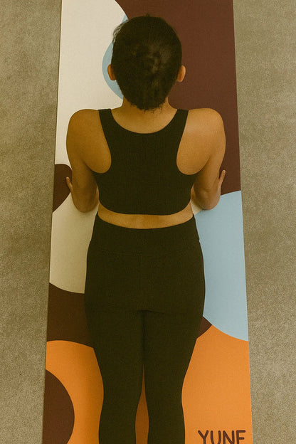 Person wearing a black athletic outfit standing on a colorful yoga mat with 'Yuna' branding.