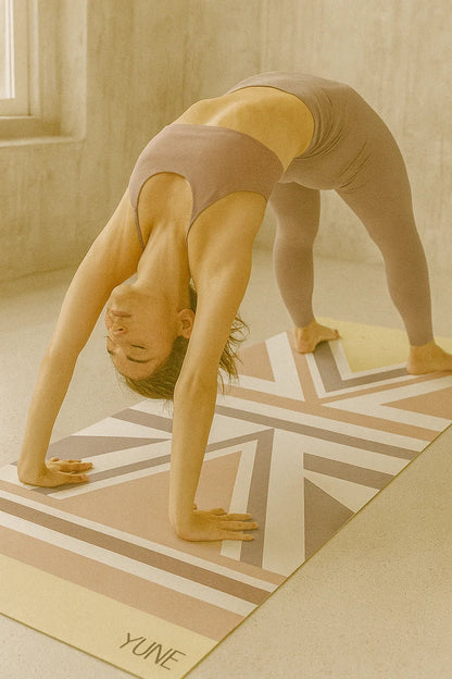 Person in a yoga pose on a YUNE mat in a room with wooden floor and window.