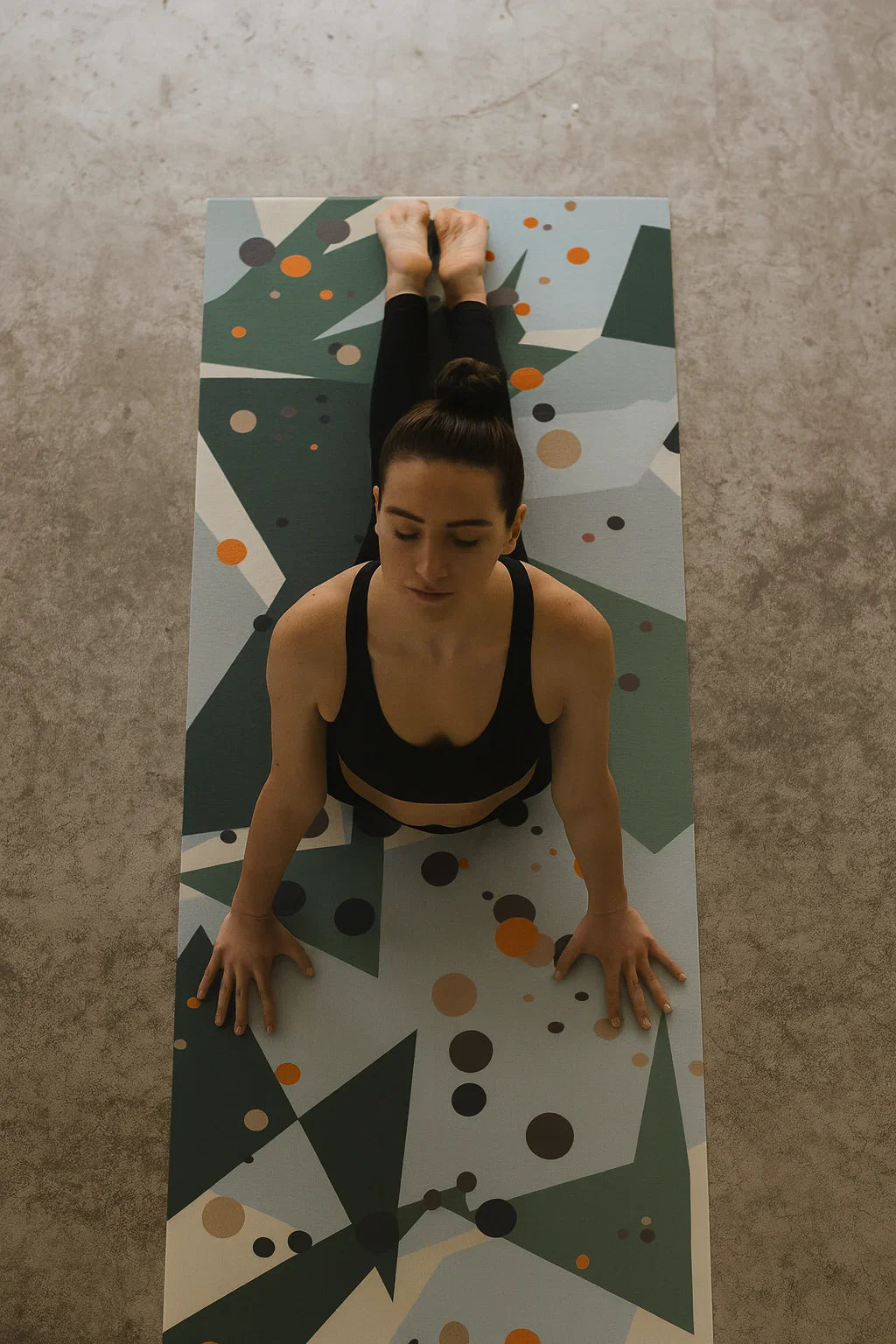 Woman practicing yoga on a patterned mat against a concrete wall.
